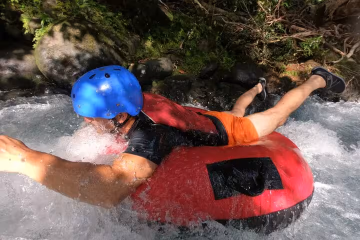 Adventurer enjoying thrilling tubing experience in Rio Celeste's clear waters, wearing safety gear and helmet.