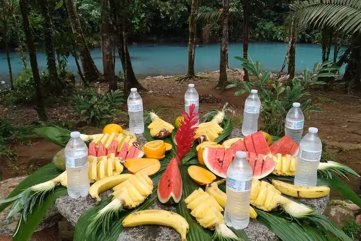 Tropical fruit and bottled water set on a leaf-covered table by Rio Celeste, enhancing the nature and adventure experience.