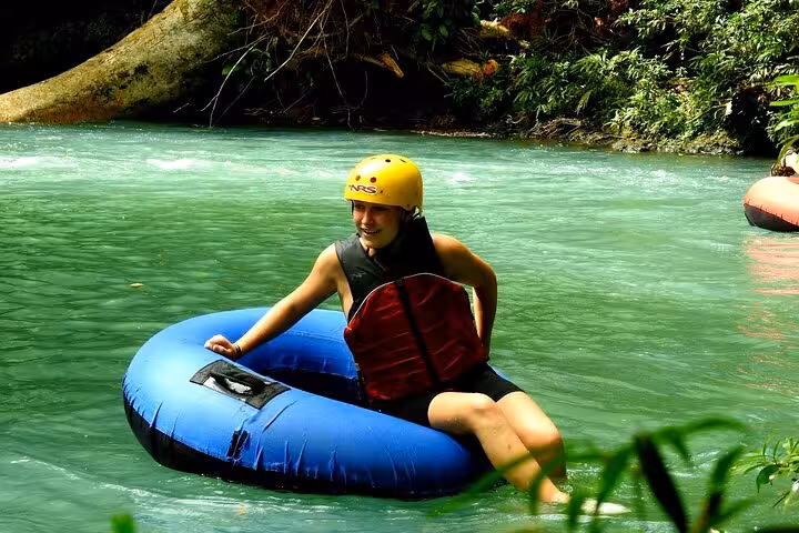 Smiling participant on a tubing adventure in Rio Celeste's turquoise waters, set against a backdrop of vibrant jungle.