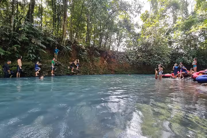 Adventurers enjoy tubing and swimming in the clear, turquoise waters of Rio Celeste amidst dense jungle scenery.