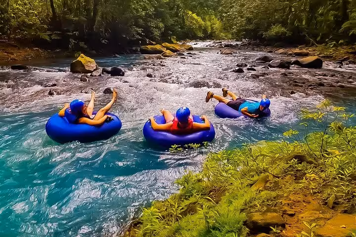 Tubers float through the vibrant blue waters of Rio Celeste, embraced by the serene rainforest landscape.
