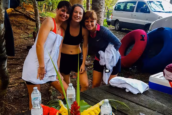 Three friends enjoying a break by the river with towels and water bottles during a tubing adventure in Rio Celeste.