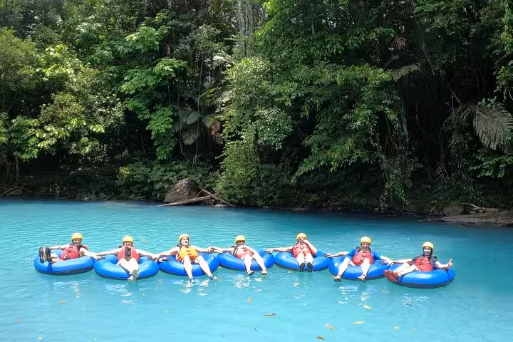 Group relaxing in tubes on the serene turquoise waters of Rio Celeste, surrounded by lush greenery.