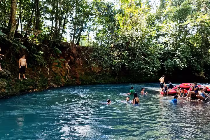 Visitors swimming in the turquoise waters of Rio Celeste, experiencing the thrill of tubing amidst tropical scenery.