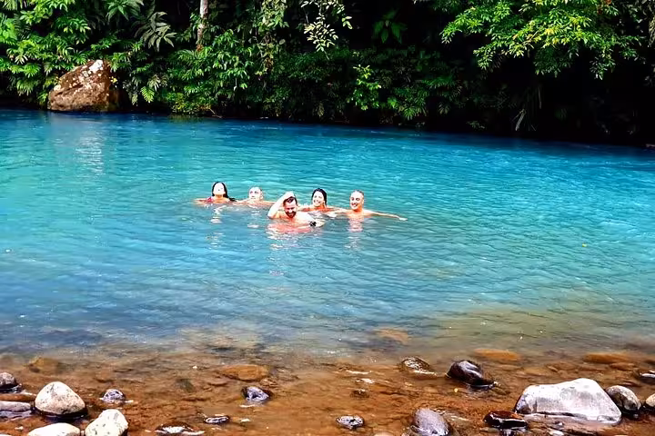 Group enjoying a refreshing swim in the pristine turquoise waters of Rio Celeste surrounded by nature.