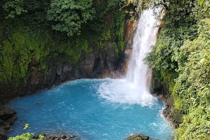 Stunning Rio Celeste waterfall cascading into vibrant turquoise waters surrounded by lush greenery.