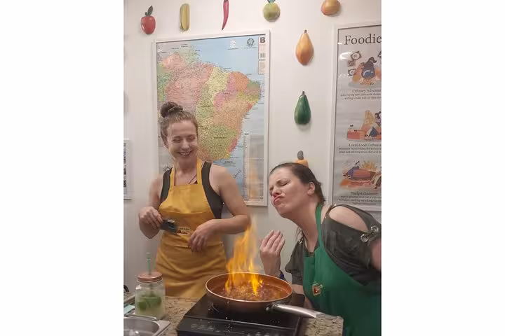 Two participants enjoying a cooking class in Rio, flambéing in a lively kitchen as part of the Cookin' Good experience.