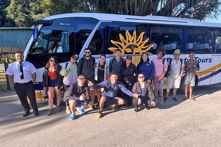 Group of happy travelers posing in front of a shuttle bus on a tour from Rio de Janeiro to Angra dos Reis.