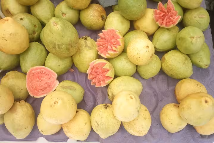 A variety of ripe guavas, some sliced to reveal pink interiors, at a bustling Rio fruit market.