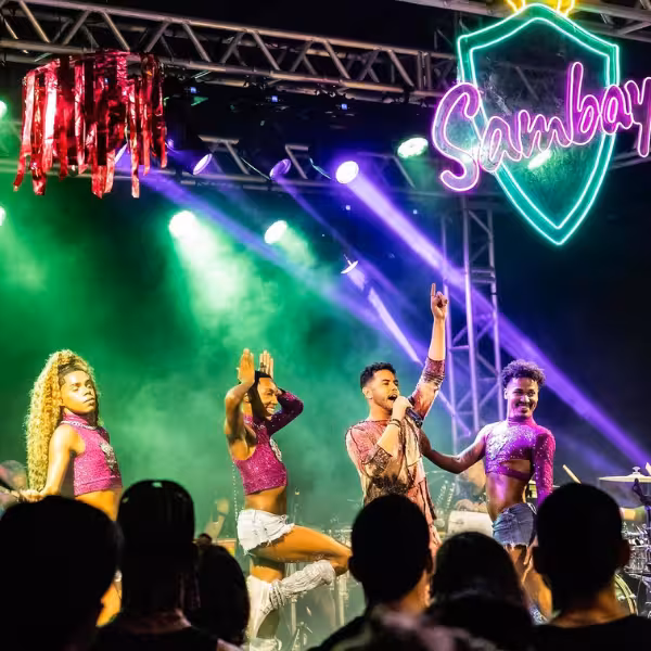Energetic samba dancers and a singer perform under vibrant lights at a Rio Gay Nightlife Experience show.