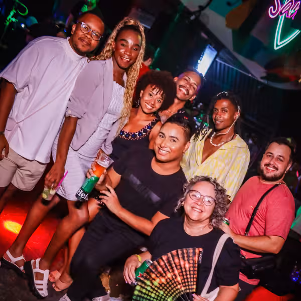 Diverse group of friends celebrating at a lively Rio Gay Nightlife event with neon lights.