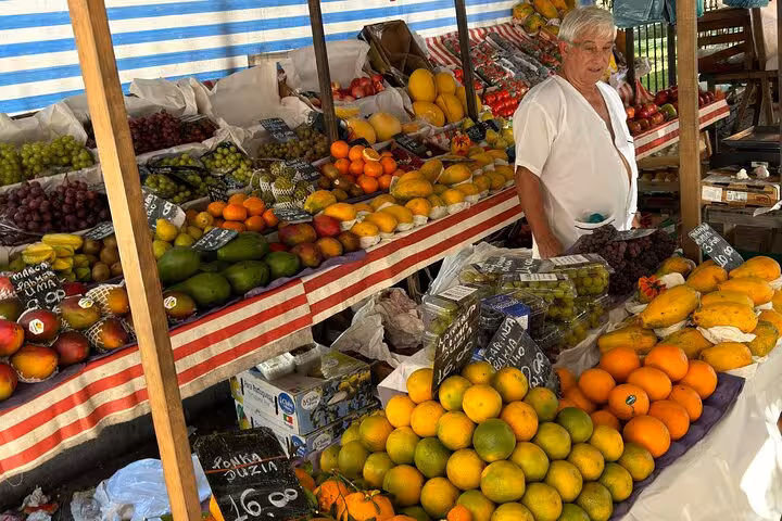 Market vendor with a colorful array of fresh tropical fruits at a bustling stall in Rio, perfect for guided tasting tours.