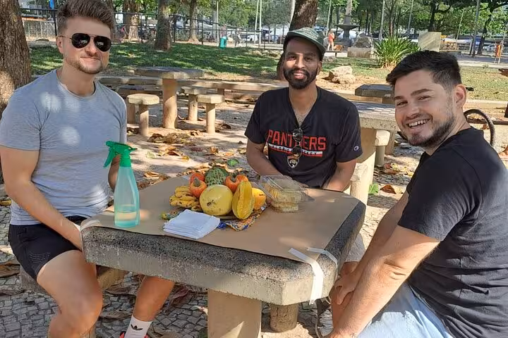 Three friends enjoying a tropical fruit tasting at a park table, part of Rio's guided market walk experience.