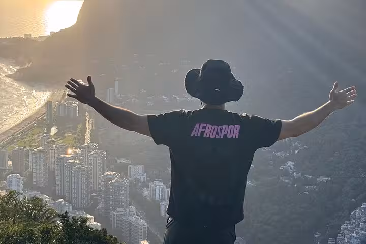 Traveler embracing sunrise atop Rio's Two Brothers with stunning cityscape below.