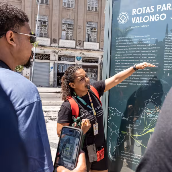 Tour guide explaining Valongo Wharf history to visitors in Rio's Little Africa area, with an informational board.