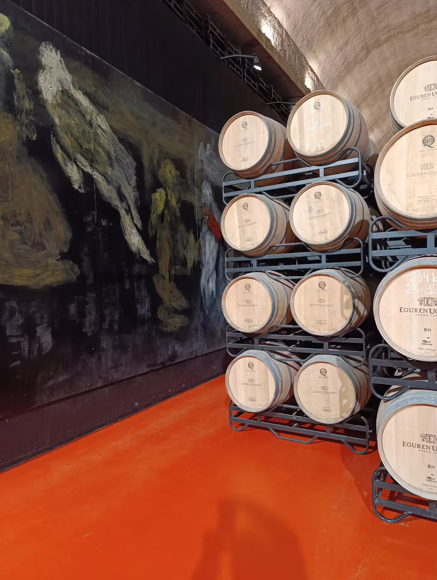 Stacked oak barrels against contemporary art mural in Rioja winery, showcasing unique blend of wine and culture.