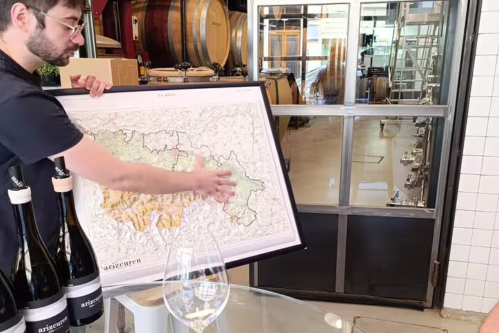 Guide explaining Rioja wine region map during a winery tour, with wine bottles and barrels in the background.