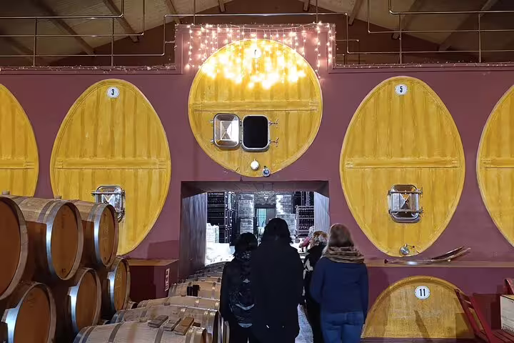 Visitors explore a Rioja winery with large wooden wine vats illuminated by warm lighting.