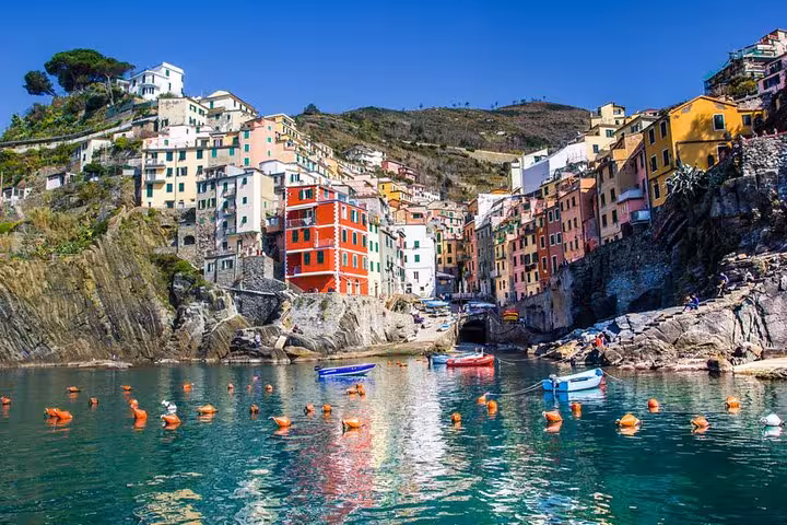 Colorful cliffside village of Riomaggiore in Cinque Terre, Italy, with boats in the turquoise harbor waters.