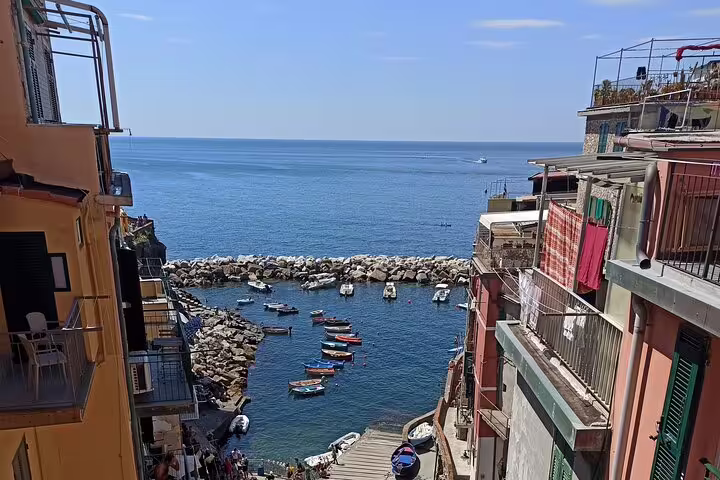 View from Riomaggiore village over narrow marina with moored boats and stone breakwater opening to the blue Ligurian Sea