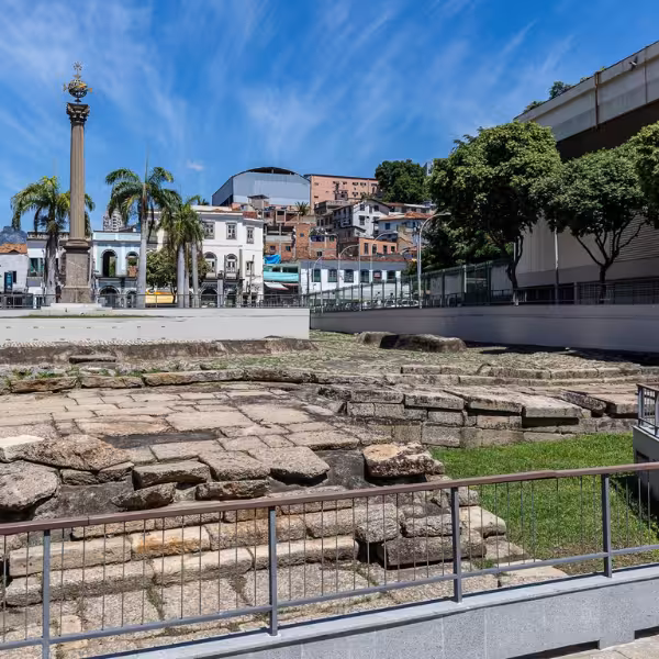 View of Rio's Valongo Wharf with historical ruins, palm trees, and vibrant cityscape under a clear blue sky.