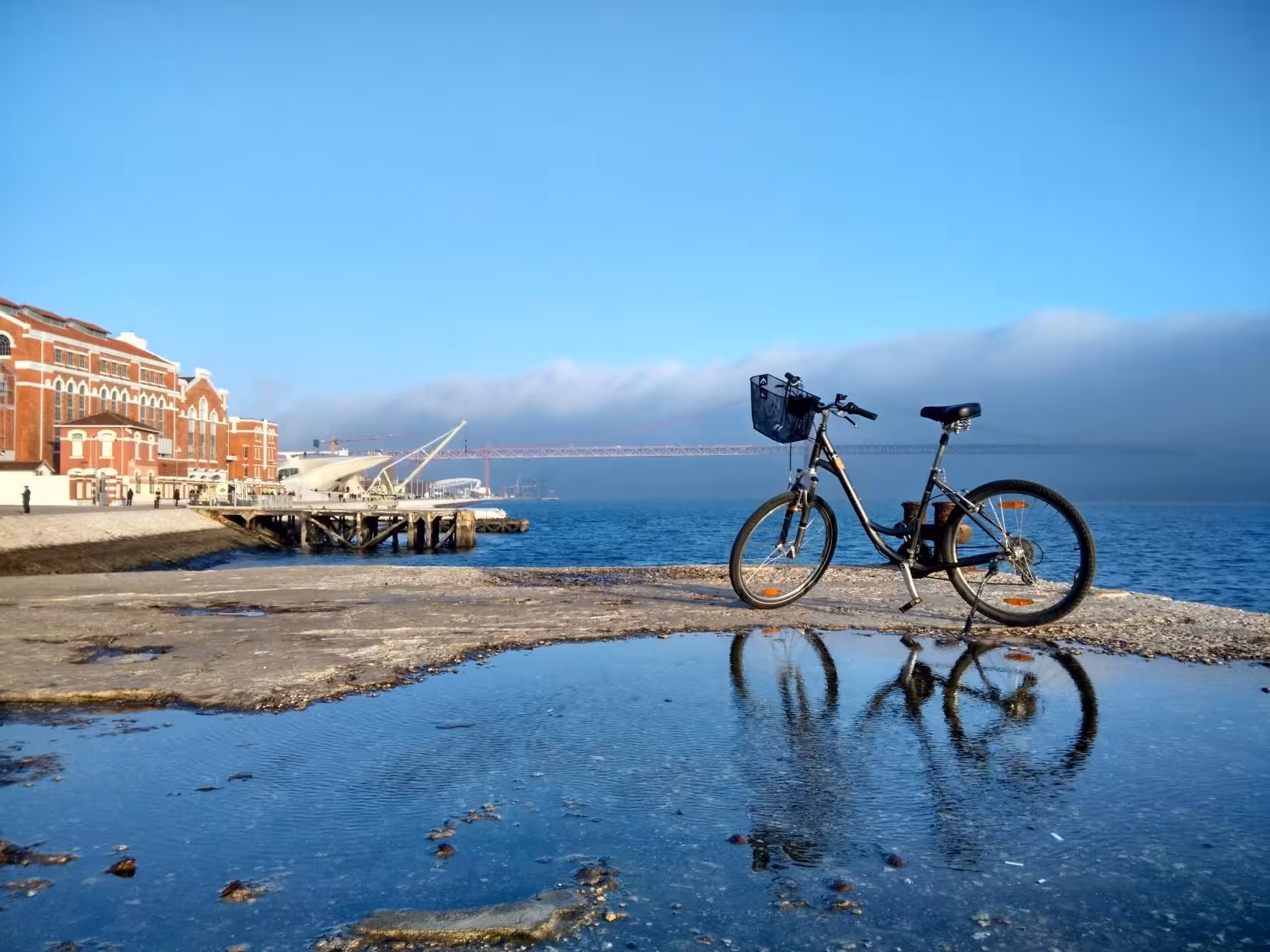 Bicycle parked by the waterfront reflecting a sunny day on the River Light Bike Tour with a bridge in the background.