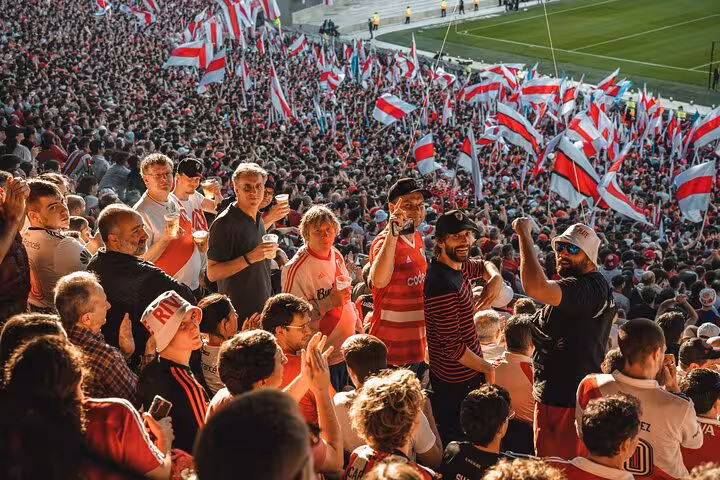 Fans cheering with drinks amid River Plate flags at El Monumental, Buenos Aires game experience with local