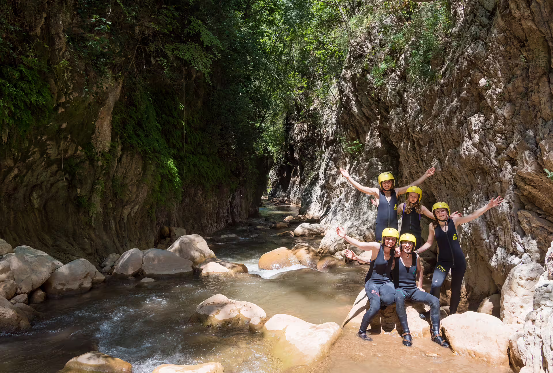 Group in wetsuits and helmets posing in Neda canyon river, a fun guided river trekking adventure in Greece