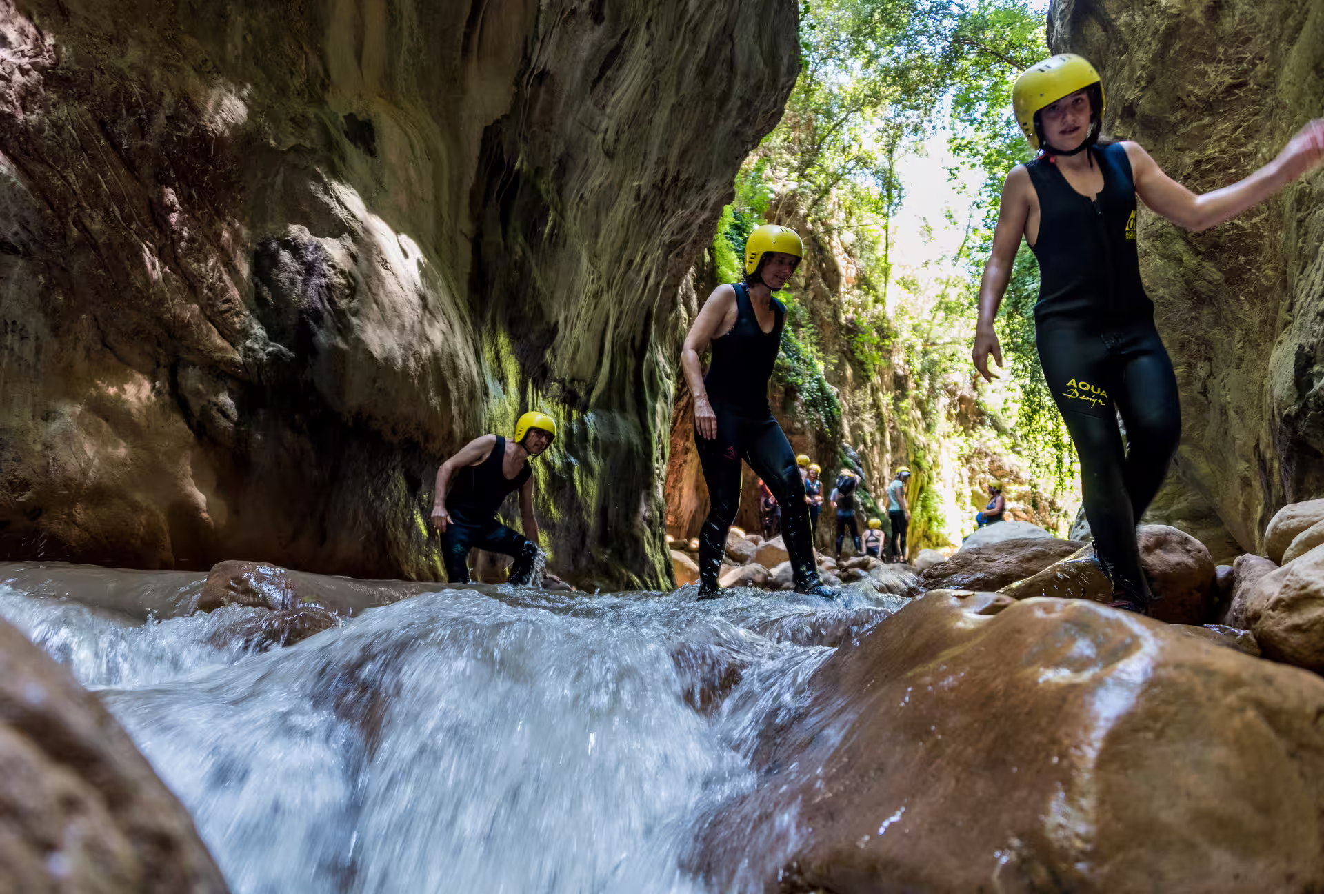 River Trekking Neda group in helmets and wetsuits wading through canyon stream on guided gorge hike