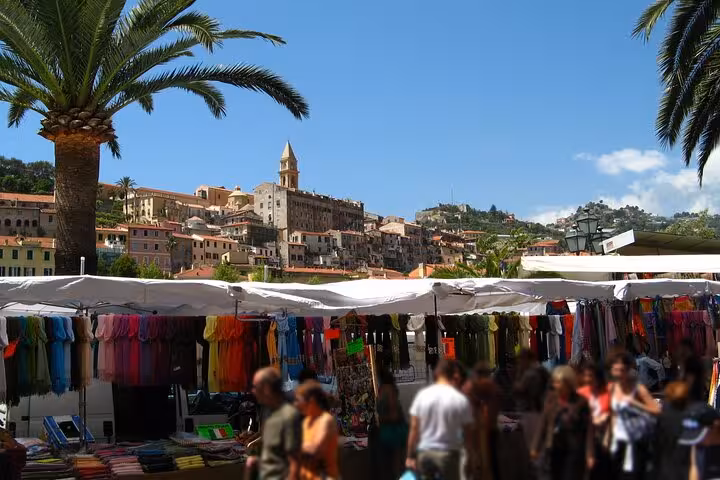 Vibrant market scene in a charming Riviera town with colorful stalls and historic architecture under sunny skies.