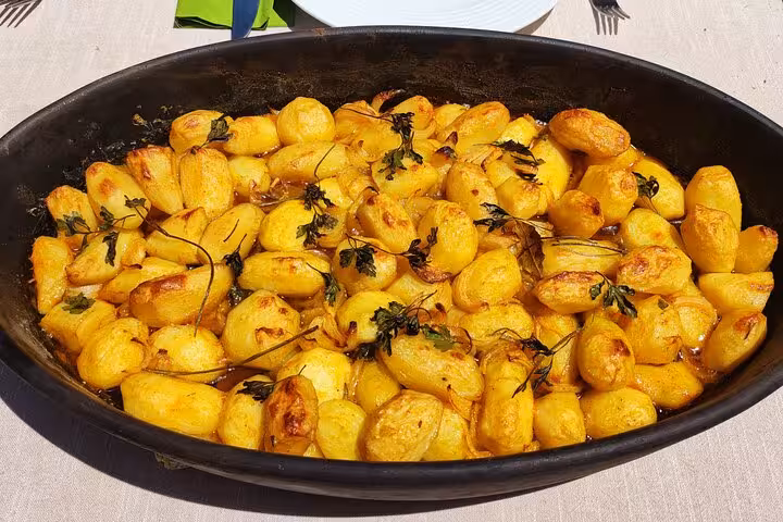 Golden roasted potatoes garnished with herbs served on a terrace during a Portuguese cooking class experience.