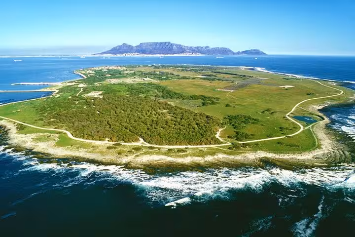 Aerial view of Robben Island, surrounded by ocean, with Cape Town and Table Mountain in the distance.