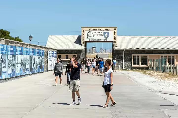 Tourists exploring the historic entrance of Robben Island under a clear blue sky on a guided full day tour.