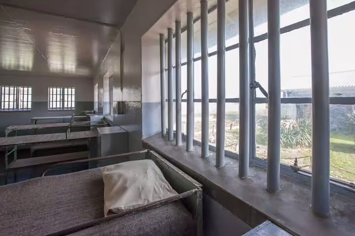 Interior view of a prison cell on Robben Island, showcasing barred windows and simple bedding, part of historic museum tour.