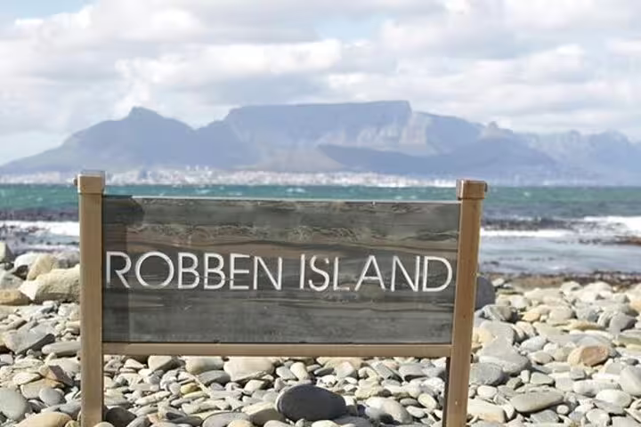 Robben Island sign with scenic ocean and Table Mountain backdrop, featured in the boat trip and museum tour.