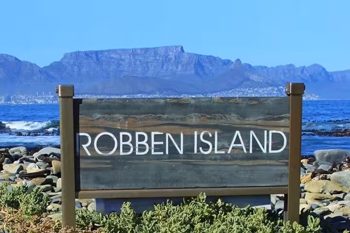 View of Robben Island sign with Table Mountain backdrop, perfect for historical tours and scenic photography.