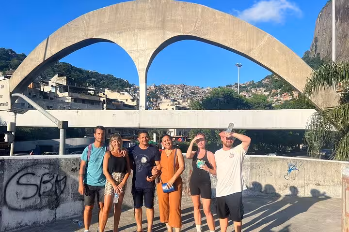 Tourists pose under an iconic arch with Rocinha favela in the background during a guided walking tour.