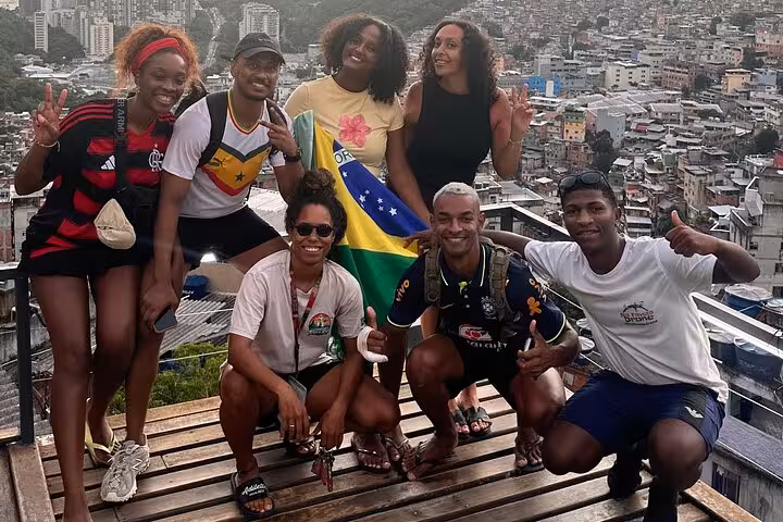 Group of tourists enjoying a panoramic view of Rocinha Favela, holding a Brazilian flag during guided tour in Rio.