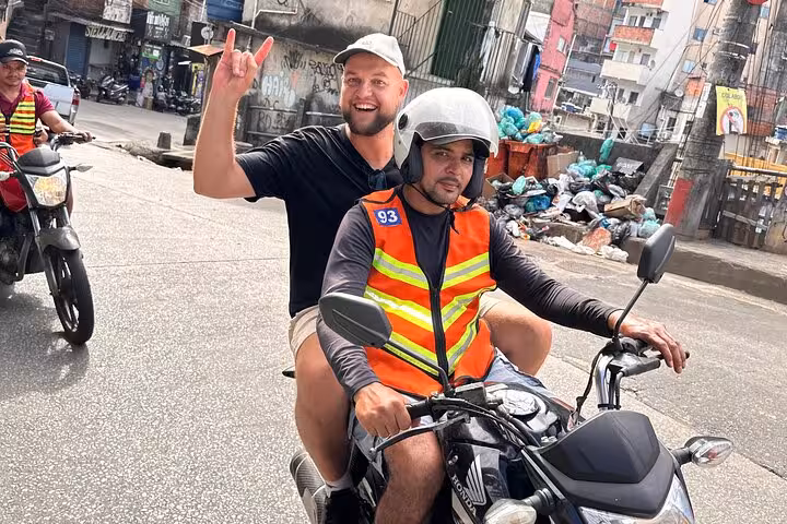 Tourist riding on a motorbike with a local guide through the vibrant streets of Rocinha favela in Rio de Janeiro.