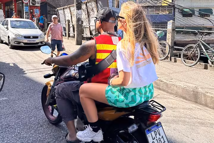 Tourist rides on a motorcycle through the vibrant streets of Rocinha favela with a local guide.