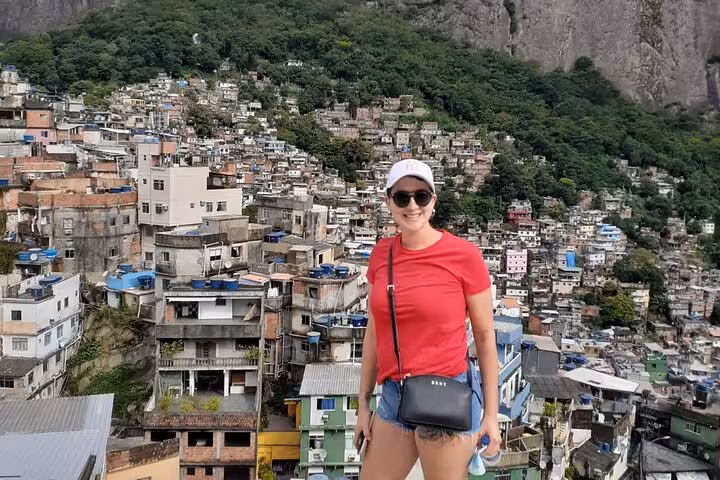 Smiling woman in front of panoramic view of Rocinha favela, showcasing the colorful, sprawling urban landscape.