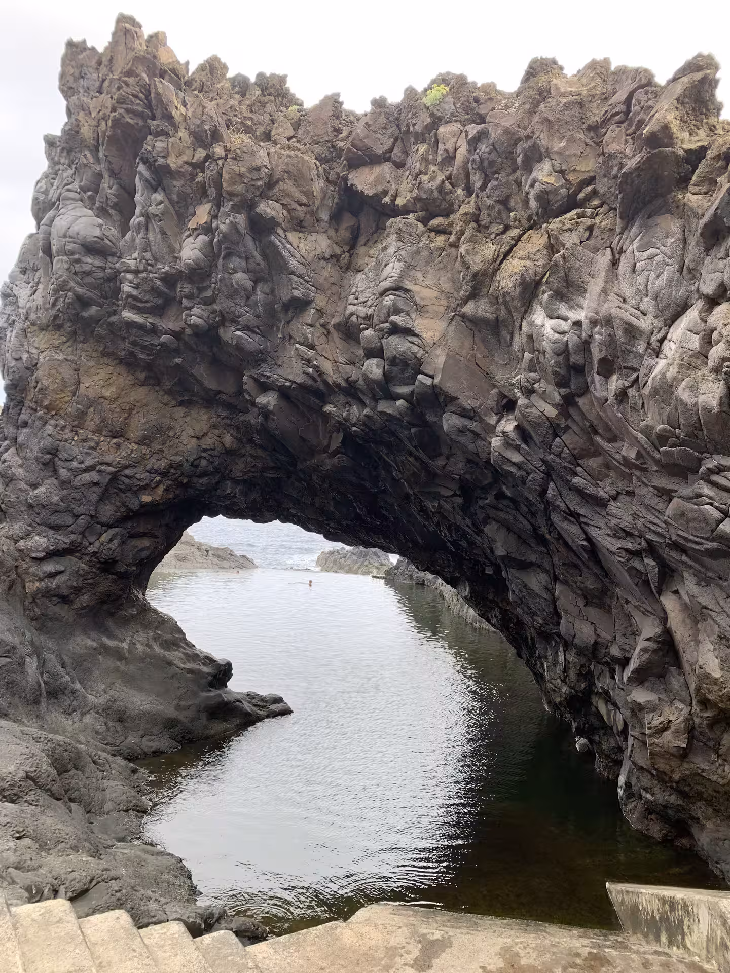 Dramatic natural rock arch formation over a tranquil water pool, featured in a private tour for small groups.