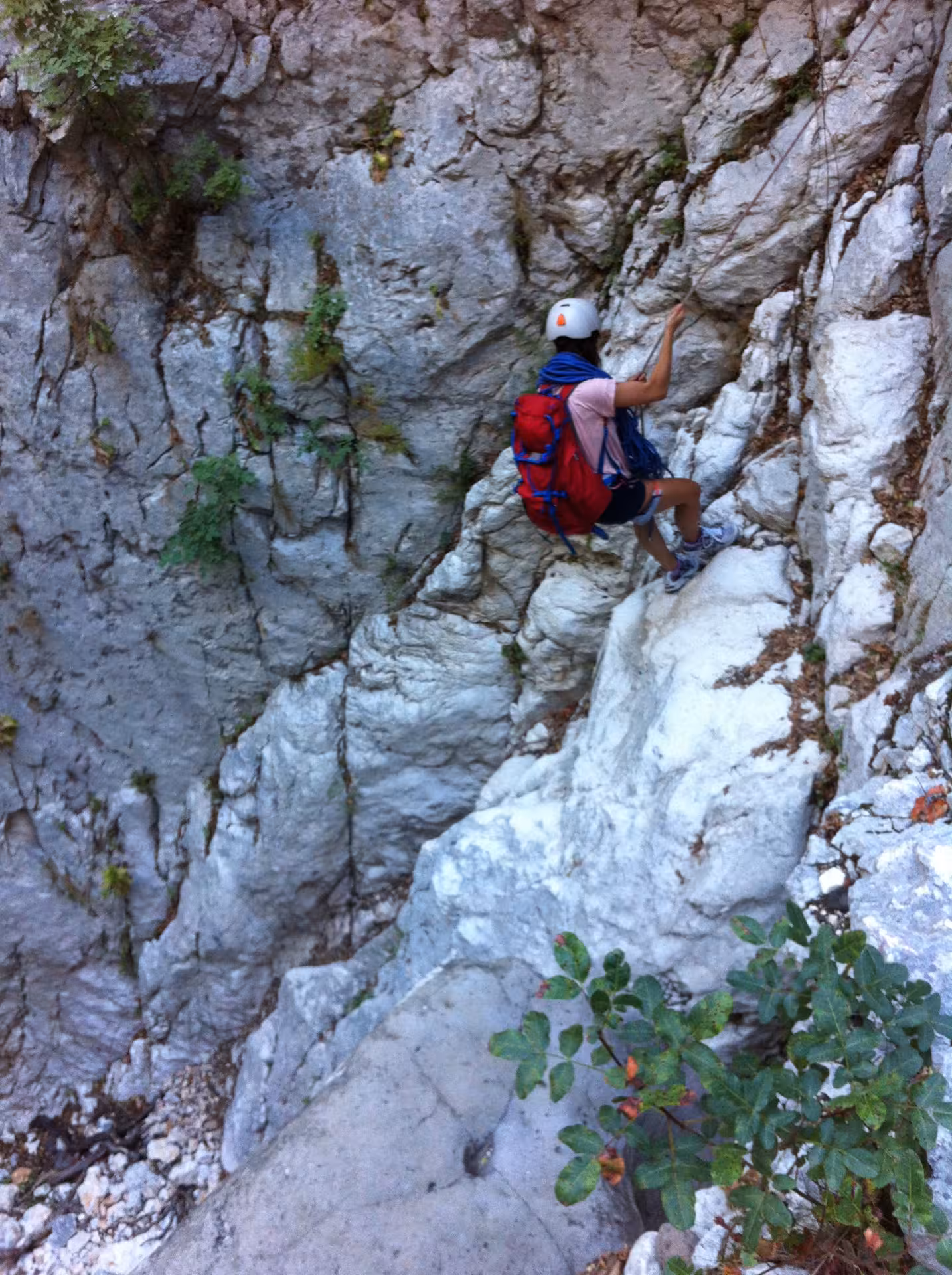 Adventurer in helmet scaling rugged rock face in Fuili Canyon, Cala Gonone, showcasing thrilling climbing experience.