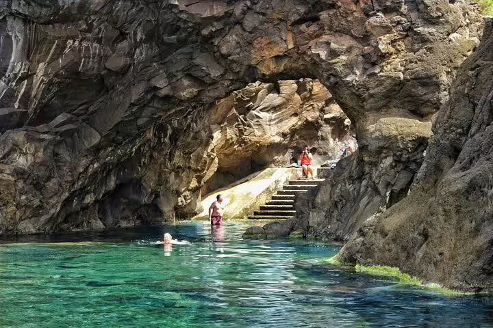 Visitors explore a stunning rocky cave with crystal-clear waters on the Private Magical Shore Excursion West tour.