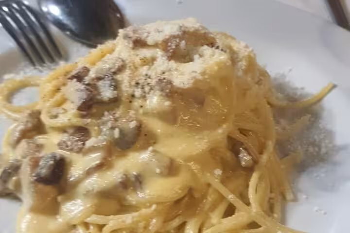Creamy carbonara pasta topped with parmesan served on a white plate, highlighting a Roman cooking class experience.