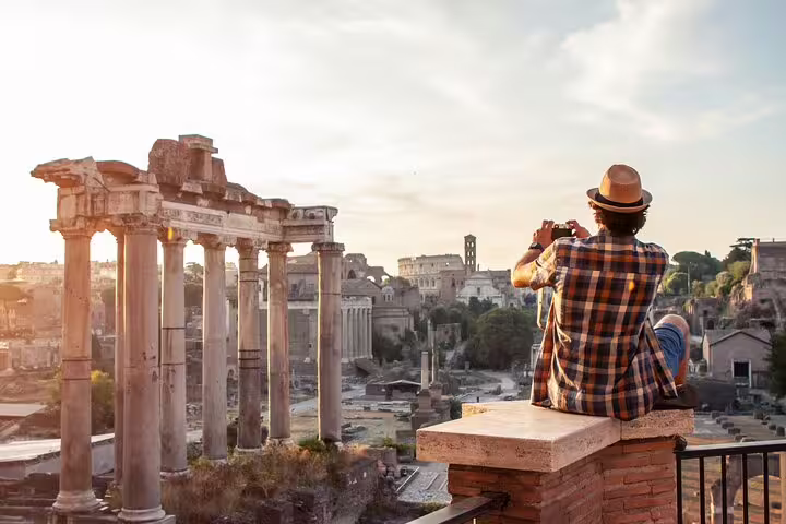 Traveler photographing the Roman Forum at sunset, capturing ancient ruins and historic landmarks in Rome, Italy.