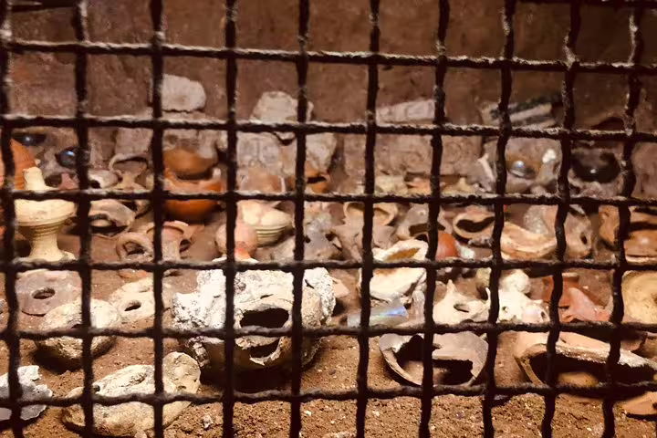 Display of excavated Roman pottery and oil lamps behind a grid in catacombs on a 2-day Rome Colosseum and Vatican tour