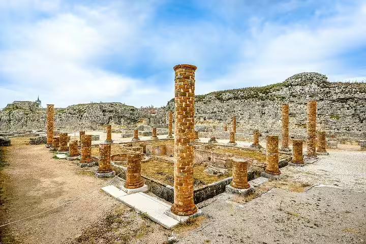 Ancient Roman ruins with brick columns under a blue sky at Conimbriga, a historic site near Fatima, Portugal tour.