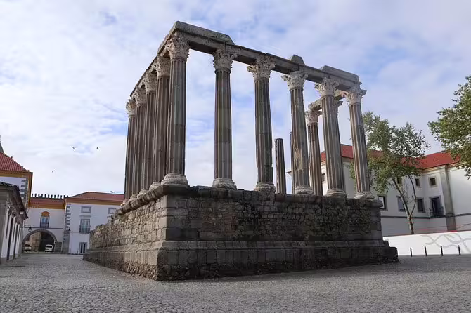 Scenic view of the ancient Roman Temple of Évora under a partly cloudy sky on a guided tour.