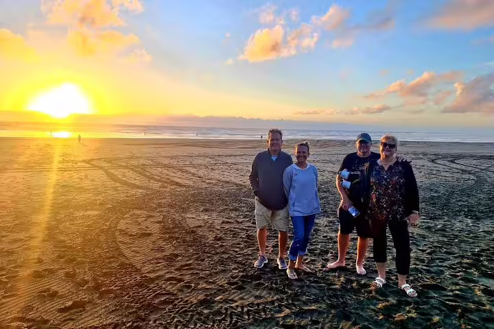 Group enjoying a romantic sunset on a sandy Auckland beach, part of a tour with winery and thermal pool delight.